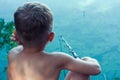 Young fisherman catches fish in river on hot summer day. boy has cast bait and is waiting for bite, sitting with his back to Royalty Free Stock Photo