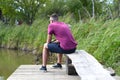 Young fisherman sitting on wooden pier, fishing in the lake. he holding the rod and looking at float Royalty Free Stock Photo