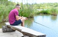 Young fisherman sitting on wooden pier, fishing in the lake. he holding the rod and looking at float Royalty Free Stock Photo