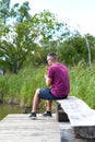 Young fisherman sitting on wooden pier, fishing in the lake. he holding the rod and looking at float Royalty Free Stock Photo