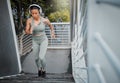 Young fit athletic mixed race woman running up stairs during outdoor workout in city while listening to music through Royalty Free Stock Photo