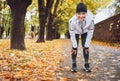 Young fit athletic smiling woman dressed modern running clothes standing and resting on knees on the footway after jogging in the