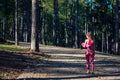 Young fit athletic woman in a forest wearing smart watch and holding yoga mat, walking away from the camera.