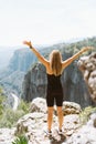 Young fit beautiful girl woman in black sporty slim outfit standing on edge of mountain cliff peak with hands up in air Royalty Free Stock Photo