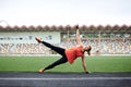 Young fit blond woman, wearing orange top and sneakers, black leggings, doing side plank, lifting her leg on stadium in summer. Royalty Free Stock Photo