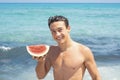 Young fit body boy portrait holding red fresh watermelon with blue ocean water in background. Summer holiday vacation season Royalty Free Stock Photo