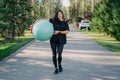 Young fit brunette woman holds big fitness ball, dressed in active wear, does exercises workout, poses in park, walks outdoor and Royalty Free Stock Photo