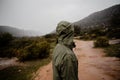 Young fit male runner resting from running on gravel mountain path in rain with rain jacket cloudy weather green bushes