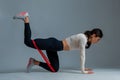 Girl doing kneeling hip extension with resistance band on grey background