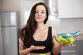 Young fit woman pointing with her hand at glass bowl full of green salad with centimeter on top ,nutrition and dietology