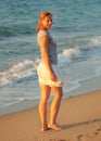 Young fit woman in short summer skirt, walking on evening beach, looking over her shoulder, afternoon sunset light shining, sea Royalty Free Stock Photo