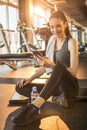 Young fit woman sitting on exercise mat and using smart-phone at gym Royalty Free Stock Photo