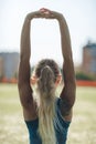 Young fitness girl in a blue shirt doing stretching in the sunset . Back view. Football field.