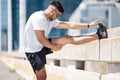 Young fitness man stretching his legs on a bridge before a run in the city. Mixed race male athlete sitting on road to