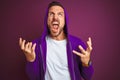 Young fitness man wearing casual sports sweatshirt and hood over purple isolated background crazy and mad shouting and yelling