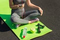 Young fitness sportswoman sitting and using smartphone in gym. Girl on yoga mat with botte of water, dumbbell and ealthy apple