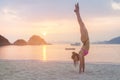 Young fitness woman doing handstand exercise on beach at sunrise. Sporty girl in bikini practicing yoga seashore. Royalty Free Stock Photo