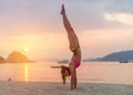 Young fitness woman doing handstand exercise on beach at sunrise. Sporty girl in bikini practicing yoga seashore. Royalty Free Stock Photo