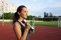 Young fitness woman holding the dumbbell and a water bottle at the stadium. Empty space Royalty Free Stock Photo