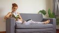 young fitness woman in sportswear doing yoga stretching leg while reading book on sofa in living room at home . sport gilr