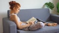 young fitness woman in sportswear doing yoga stretching leg while reading book on sofa in living room at home . sport gilr