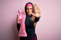 Young fitness woman wearing sport clothes and towel drinking water from take away bottle with open hand doing stop sign with Royalty Free Stock Photo