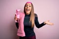 Young fitness woman wearing sport clothes and towel drinking water from take away bottle very happy and excited, winner expression