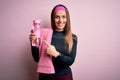 Young fitness woman wearing sport clothes and towel drinking water from take away bottle very happy pointing with hand and finger