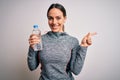 Young fitness woman wearing sport workout clothes drinking water from plastic bottle very happy pointing with hand and finger to