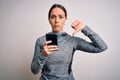 Young fitness woman wearing sport workout clothes using smartphone app with angry face, negative sign showing dislike with thumbs Royalty Free Stock Photo