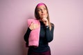 Young fitness woman wearing sport workout clothes using towel over pink background serious face thinking about question, very Royalty Free Stock Photo