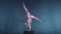 Young flexible blonde circus acrobat posing in studio in costume. Doing equilibre balance handstand on a cube.