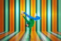 Young flexible sportive man dancing breakdance in green and blue sport uniform outfit against striped studio background.