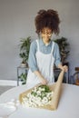 Young florist in apron creating beautiful simple daisy bouquet in craft paper Royalty Free Stock Photo