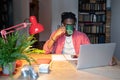 Young focused African American man freelancer drinking coffee from mug sits at work desk with laptop Royalty Free Stock Photo