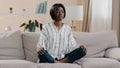 Young focused african american woman sitting in lotus position with closed eyes healthy calm girl relaxing on sofa Royalty Free Stock Photo