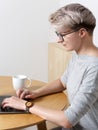 Young focused hipster millennial female with short blonde haircut working with laptop in cafe interior