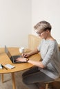 Young focused hipster millennial female with short blonde haircut working with laptop in cafe interior