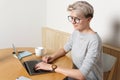 Young focused hipster millennial female with short blonde haircut working with laptop in cafe interior