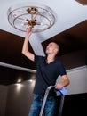 A young, focused man is replacing a lamp in a chandelier. Royalty Free Stock Photo