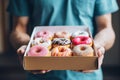 A young food delivery guy holds a craft cardboard box of colorful fresh sweet donuts with different flavors. An Royalty Free Stock Photo