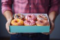 A young food delivery guy holds a craft cardboard box of colorful fresh sweet donuts with different flavors. An Royalty Free Stock Photo