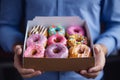 A young food delivery guy holds a craft cardboard box of colorful fresh sweet donuts with different flavors. An Royalty Free Stock Photo