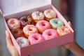 A young food delivery woman holds a craft cardboard box of colorful fresh sweet donuts with different flavors. An Royalty Free Stock Photo