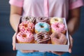 A young food delivery woman holds a craft cardboard box of colorful fresh sweet donuts with different flavors. An Royalty Free Stock Photo