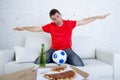 Young football fan man watching game on tv in team jersey celebrating goal crazy happy on couch