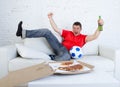 Young football fan man watching game on tv in team jersey celebrating goal crazy happy on couch