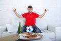 Young football fan man watching game on tv in team jersey celebrating goal crazy happy on couch