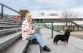 Young freelance expat woman sitting on the stairs of office building drinking coffee and working on laptop computer with her dog Royalty Free Stock Photo