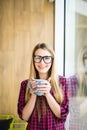 Young freelance lady drinking coffee in casual clothes and looking at camera near a window. Morning. Royalty Free Stock Photo